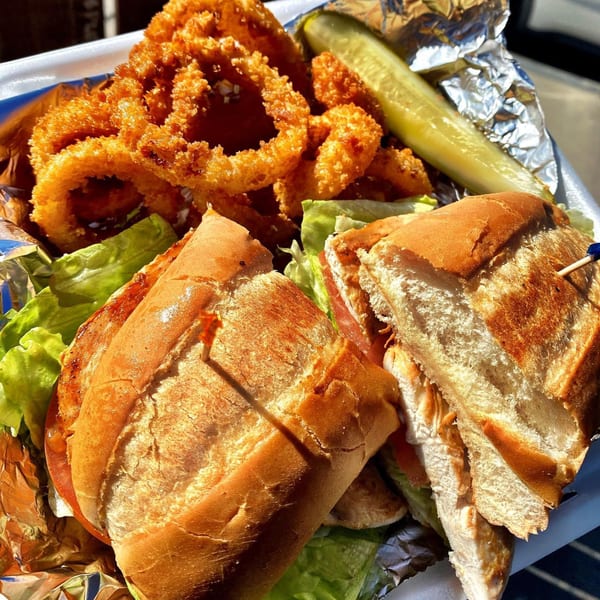A close-up of a sandwich with lettuce and tomato, golden onion rings, and a pickle spear.