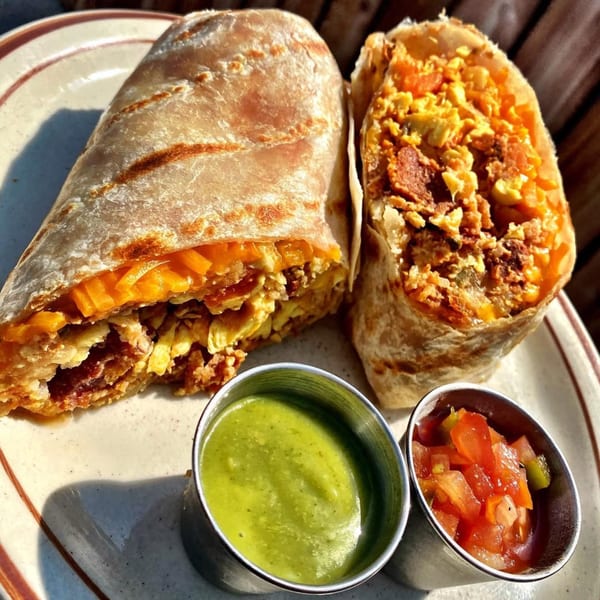 Two breakfast burritos filled with eggs, cheese, and bacon, served with green salsa and pico de gallo.