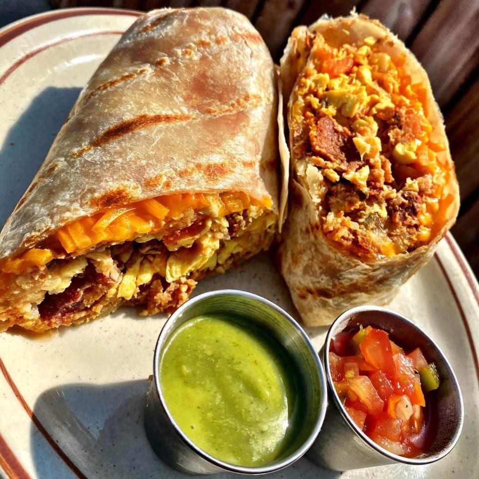 Two breakfast burritos filled with eggs, cheese, and bacon, served with green salsa and pico de gallo.