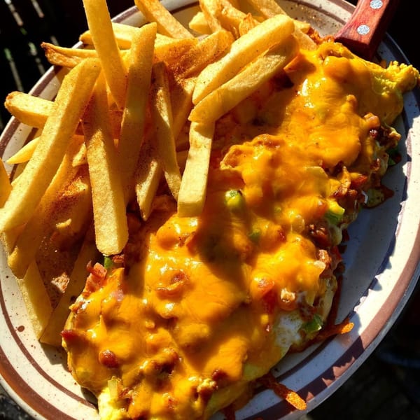 A plate of golden french fries next to a chili cheese omelet with melted cheddar.