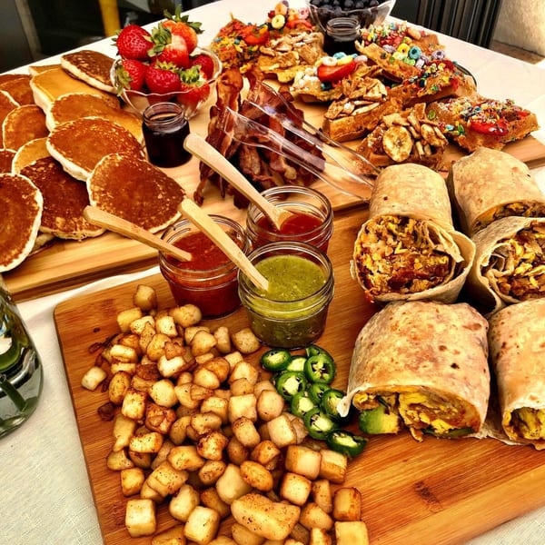 A breakfast spread with pancakes, waffles, bacon, breakfast burritos, home fries, and salsas.
